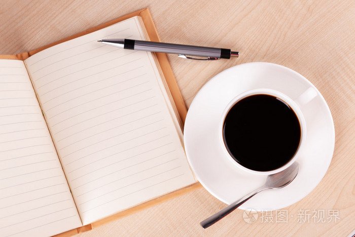 杯咖啡碟与打开笔记本和笔在木桌背景上
