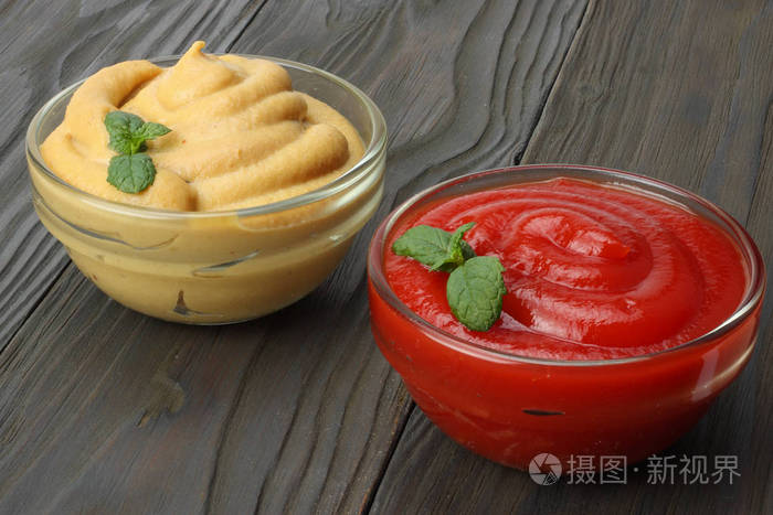 在玻璃碗里木背景上的芥末番茄酱表