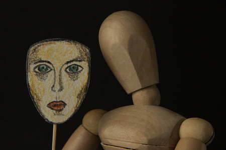 在转轴上的木制娃娃手里拿着一个面具和覆盖她的脸