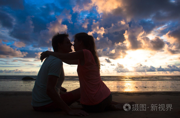 夕阳西下的一对相爱的年轻夫妇拥抱和亲吻的剪影