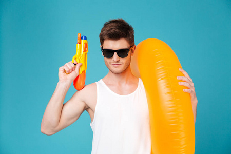 年轻男子拿着水枪和充气环的太阳镜照片