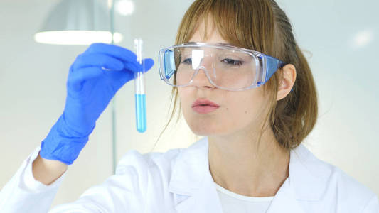女性研究科学家，医生看着蓝色溶液在试管中
