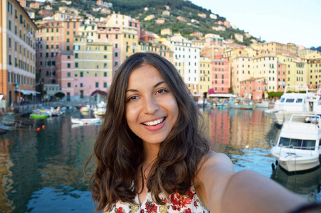 幸福的年轻女人晒黑采取自拍照照片中典型的意大利景观与海港和多彩的房屋的意大利假期在利古里亚，意大利