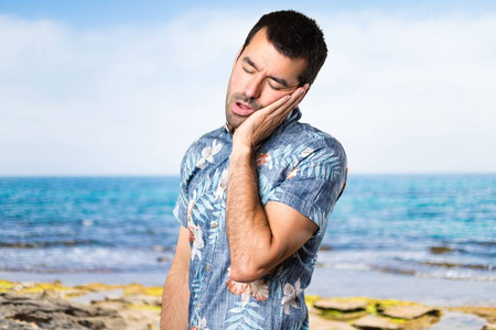 英俊的男人，与花衬衫制作睡眠姿势在海滩