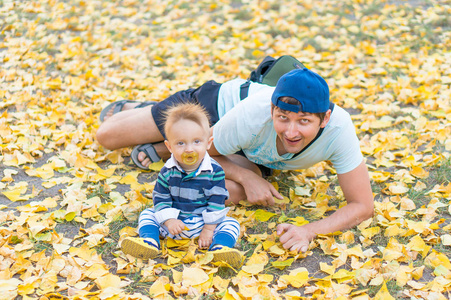快乐的父亲，和黄色的叶子在公园里玩的小男婴。秋天