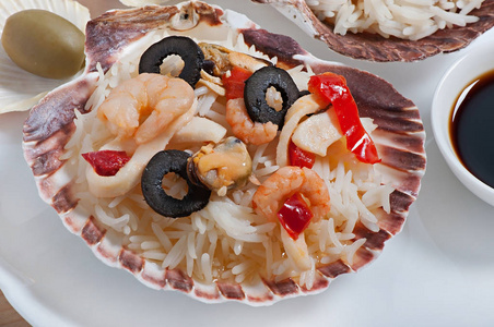 在贝壳中, 用海鲜虾贻贝鱿鱼环和橄榄装饰的大米。膳食食品