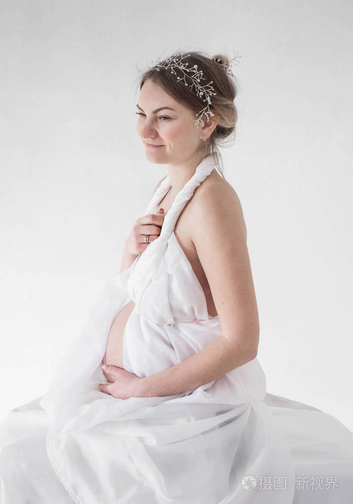 照片肖像的一个怀孕的女孩在一个白色的王冠白色的窗帘在一个侧面的