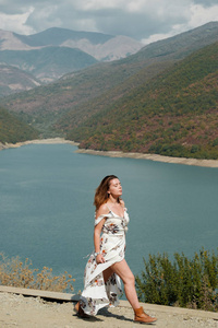 美丽的女孩在一条长的礼服在湖和山的背景