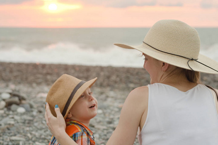 妈妈和儿子在鹅卵石海滩上休息。日落时间。后退视图