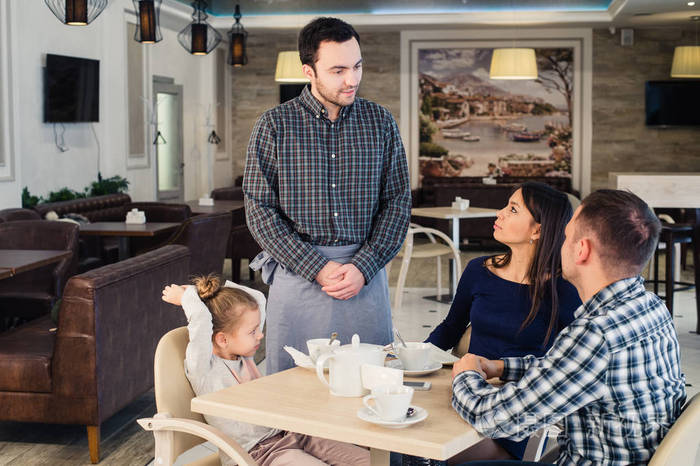 餐厅和假日概念-菜单给幸福的家庭,在咖啡厅的服务员