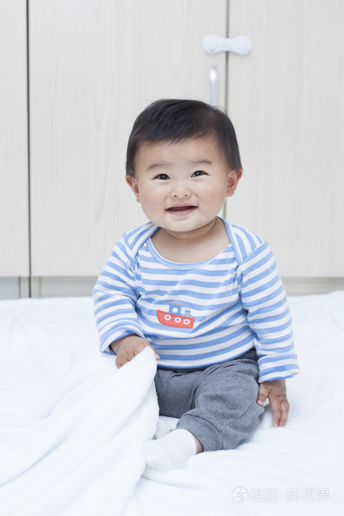 可爱的中国娃娃小男孩坐在一条白色的毯子