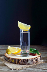伏特加或龙舌兰酒在玻璃杯中, 并在瓶子与柠檬 slie 在质朴的木质背景。传统的强力饮品。垂直视图