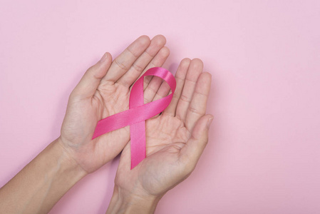 女性手捧粉红色缎带乳腺癌的粉红色背景
