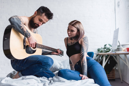 纹身男友在卧室里为女朋友弹吉他