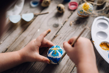 娃娃手的裁剪视图在木桌上用蓝色和黄色的颜色在花主题中着色鸡蛋