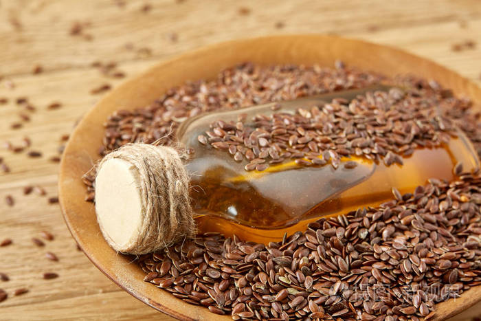 顶部视图特写图片胡麻种子和亚麻籽油在一个玻璃瓶子上的木质背景浅