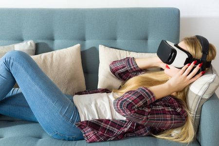 有魅力的女人戴上虚拟现实眼镜躺在沙发上。虚拟现实耳机。生活方式虚拟现实的概念