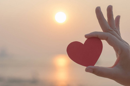 女子手捧红纸心在沙滩上照片
