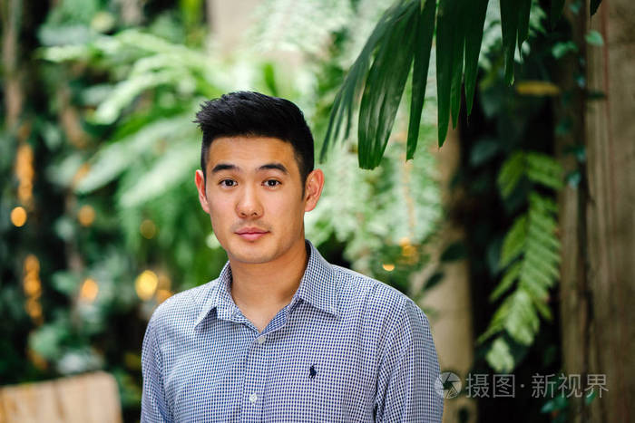 一个英俊, 年轻, 聪明的中国亚裔男子的肖像微笑着, 站在绿色的墙上的