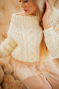 美丽的年轻女子穿着漂亮的毛衣摆在米色背景。时尚照片