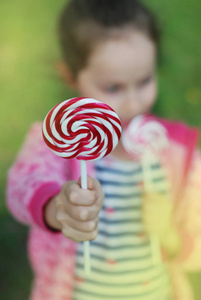 关闭漩涡糖果 Lolipop 握由小女孩在绿色庭院甜糖红色糖果