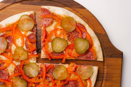 用番茄酱芝士干酪意大利辣香肠甜椒和泡菜在木制披萨盘上的切片比萨饼特写