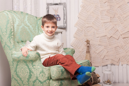 在圣诞节室内椅子上的小微笑的男孩