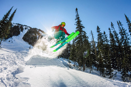 滑雪者 freerider 跳从太阳雪匝道上的山川 森林背景