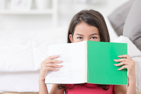 快乐的亚洲女孩与绿色书掩藏自己在书之后