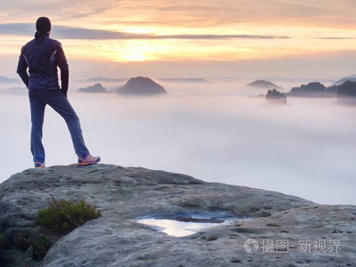 男子站独自在岩石的山峰上望着秋天太阳在地平线上的徒步旅行者美丽的