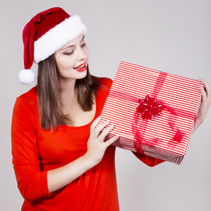 红色的裙子和圣诞老人的帽子的黑发女人拥着礼物并在相机看