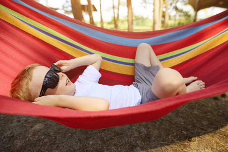 性格开朗的小男孩带着太阳眼镜躺在吊床上，在一片松树林，他自然在休息和看向天空
