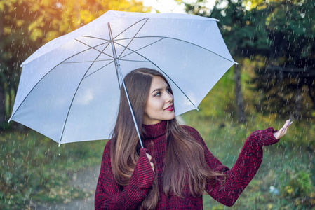 快乐的年轻女子在阳光明媚的公园里散步, 在雨中带着一把白色的雨伞.