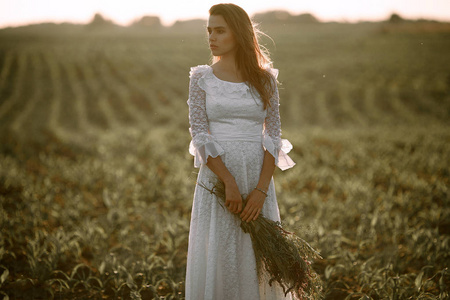 年轻女子在长长的白色花边礼服上的麦田