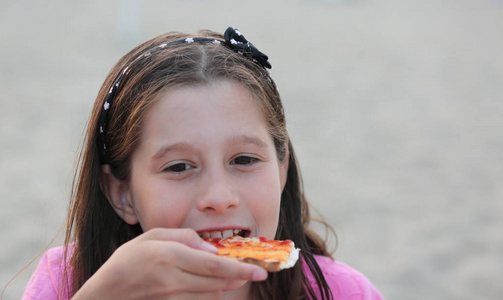 白种人的小女孩在海滩上吃披萨