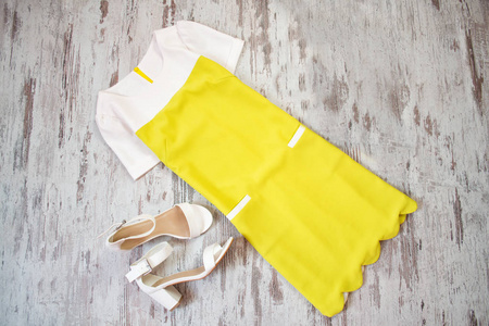 黄色和白色的衣服，白色鞋在木制的背景上。时尚概念，顶视图