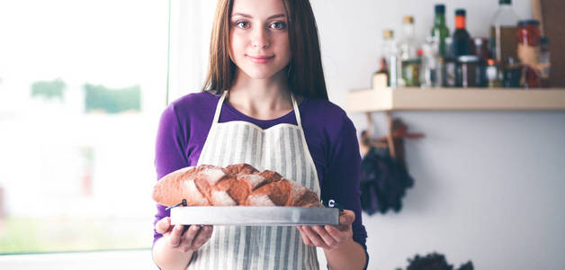 一个年轻的女子站在她的厨房里拿着面包
