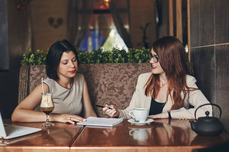 两个年轻的白种人女企业家与笔记本电脑。在咖啡馆中的妇女