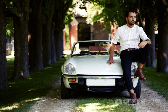 坐在豪华敞蓬车引擎盖上的男人