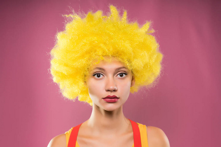 伤心的女孩小丑在粉红色的背景上的黄色假发