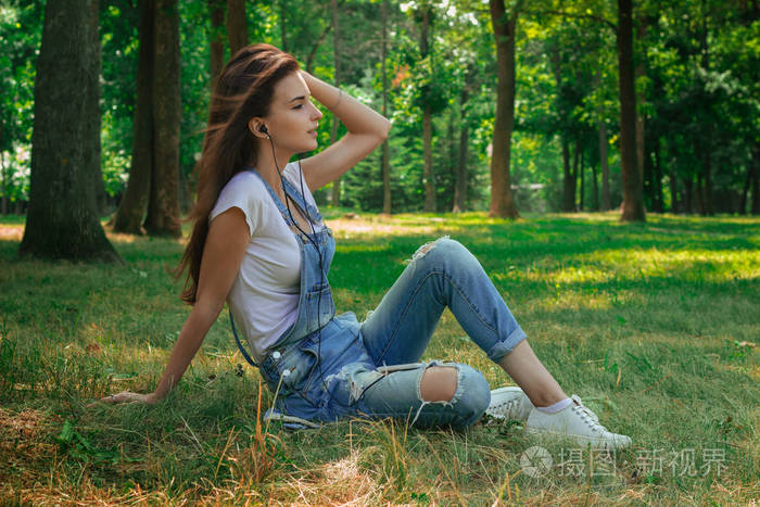年轻可爱的女孩坐在草地上听音乐
