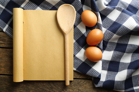 打开食谱书 鸡蛋和餐巾放在木制的背景