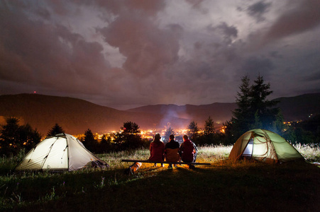 坐在帐篷附近篝火周围用木板上的三名游客