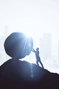 背光的推巨石上山的商人形象.与阳光明亮的背景.挑战概念照片