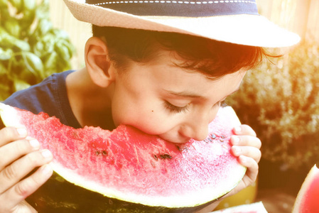 可爱的男孩儿童与巴拿马杯吃健康的有机食品，西瓜。自然背景，阳光灯