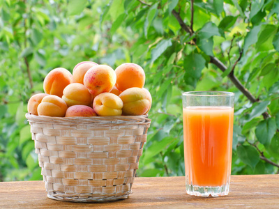 杏子在柳条篮子和一杯果汁的绿色背景，阳光