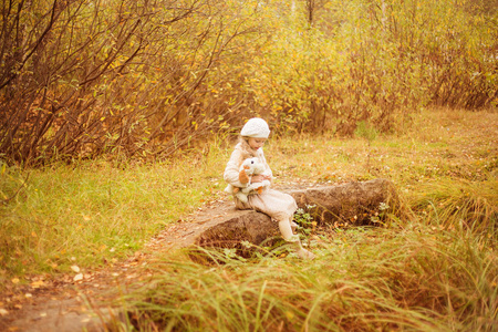 可爱的女孩，有长长的卷发正坐在一块大石头与最喜欢的玩具，在秋天的公园
