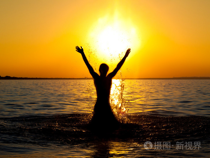 游泳者在金色的夕阳上跳海水
