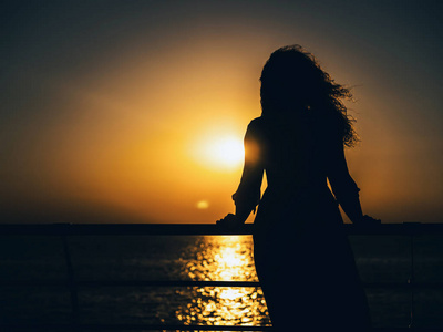 夏天裙子快乐的女人夏天穿裙子在夕阳西下的时候站在海边的剪影.