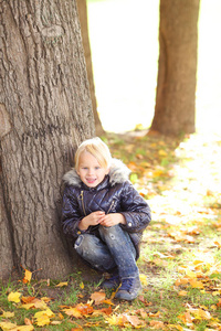 男孩坐在树下在秋天的公园